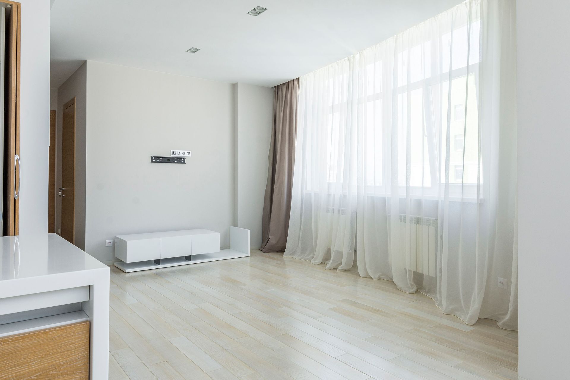 Bright modern minimalist apartment interior with large windows and sheer curtains.