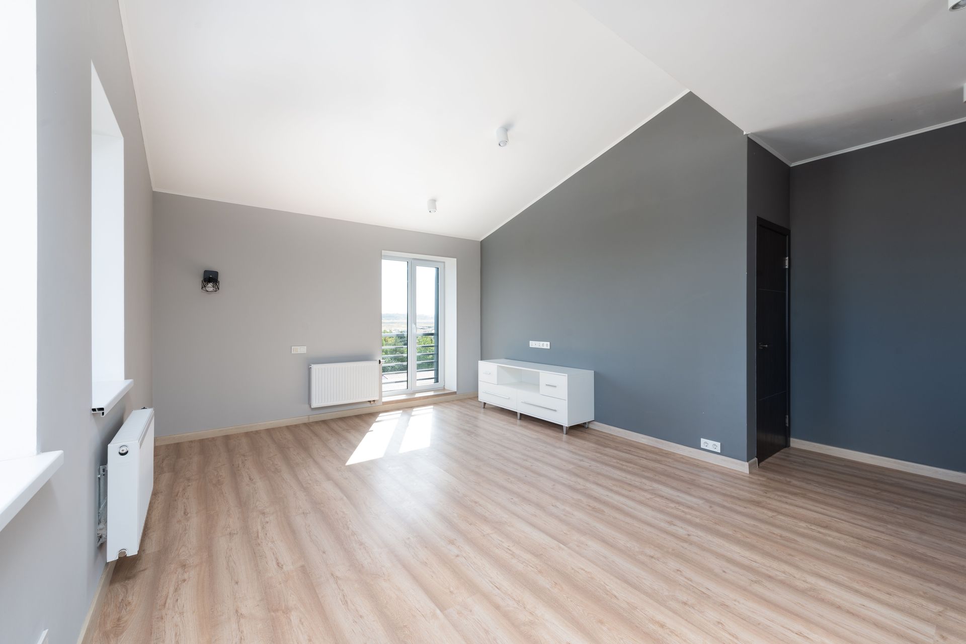 Wide-angle shot of a modern unfurnished apartment with wooden flooring and large windows.